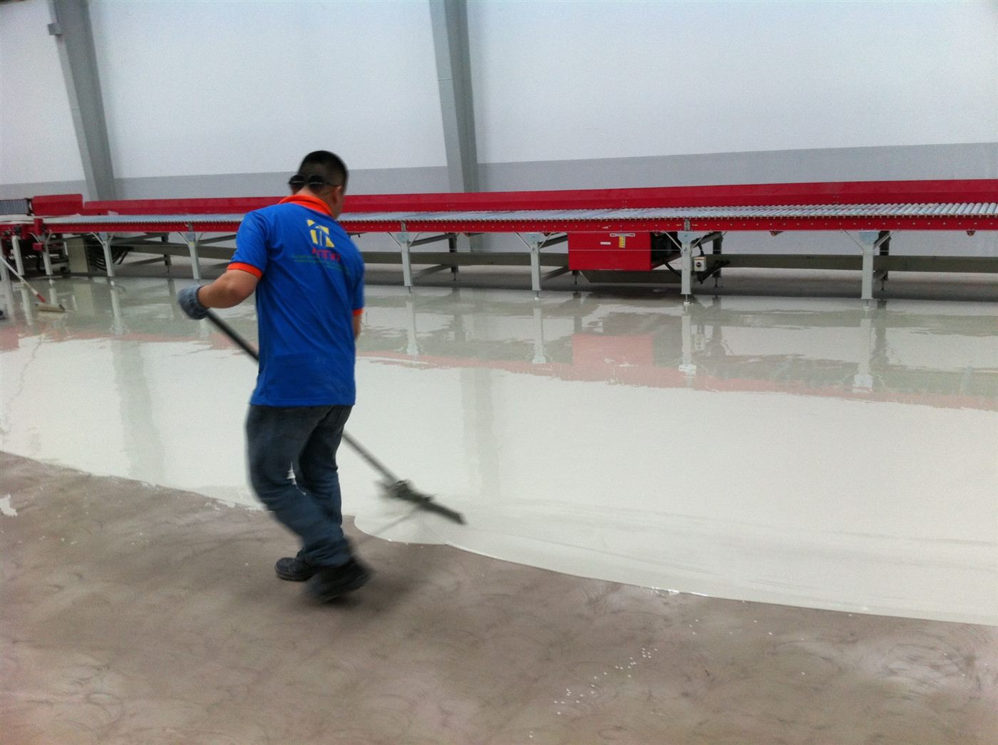 Kỹ thuật viên ANTINCORP san phẳng lớp epoxy bên cạnh băng chuyền tại kho DHL